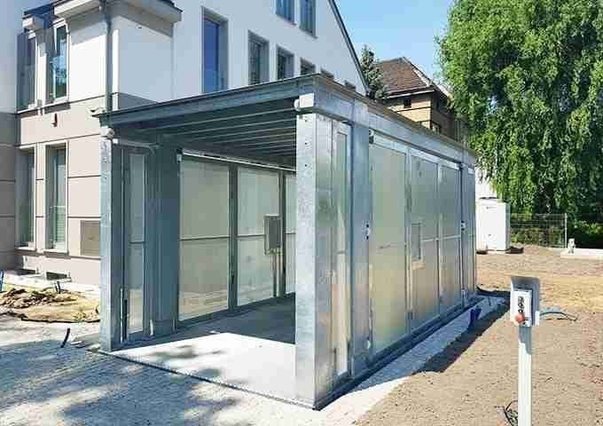 Struttura metallica moderna con porte scorrevoli in vetro e finestre collegata a casa residenziale bianca, giardino con prato e alberi sullo sfondo